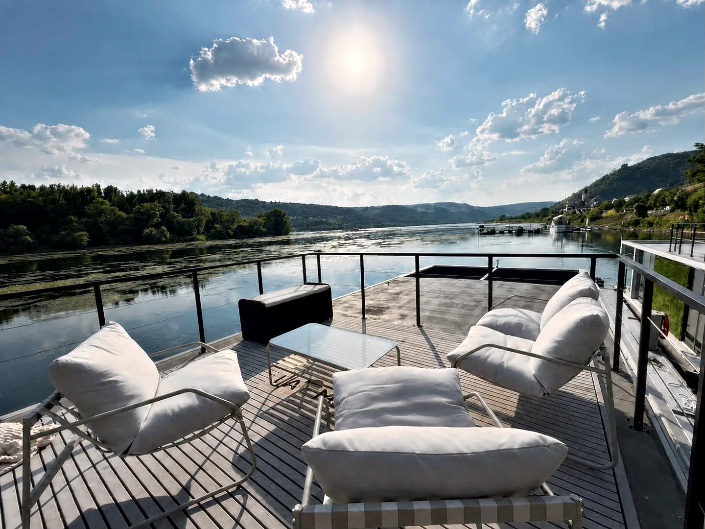 Die Dachterrasse von Modern 1: helle Loungesessel und ein niedriger Tisch auf dem Oberdeck, davor der Rhein und die Hänge des Mittelrheintals.