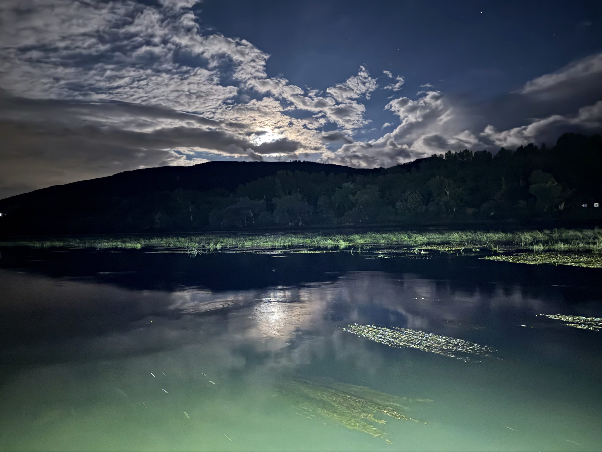 Nachthimmel über dem Rheintal: aufgerissene Wolken, dahinter Sterne, das Mondlicht spiegelt sich im stillen Wasser der Marina.