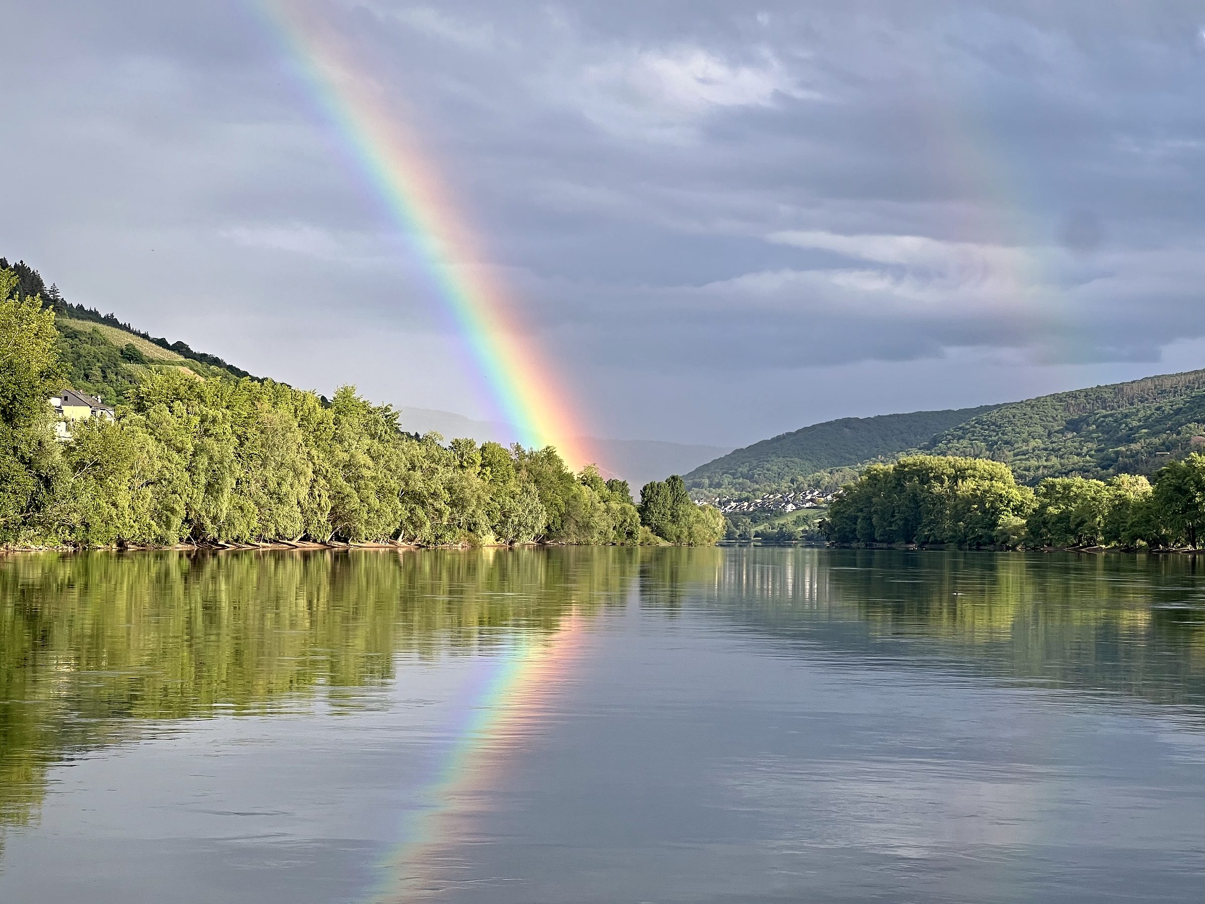 Doppelter Regenbogen über dem Rhein bei Lorch, gespiegelt im ruhigen Wasser zwischen bewaldeten Ufern.