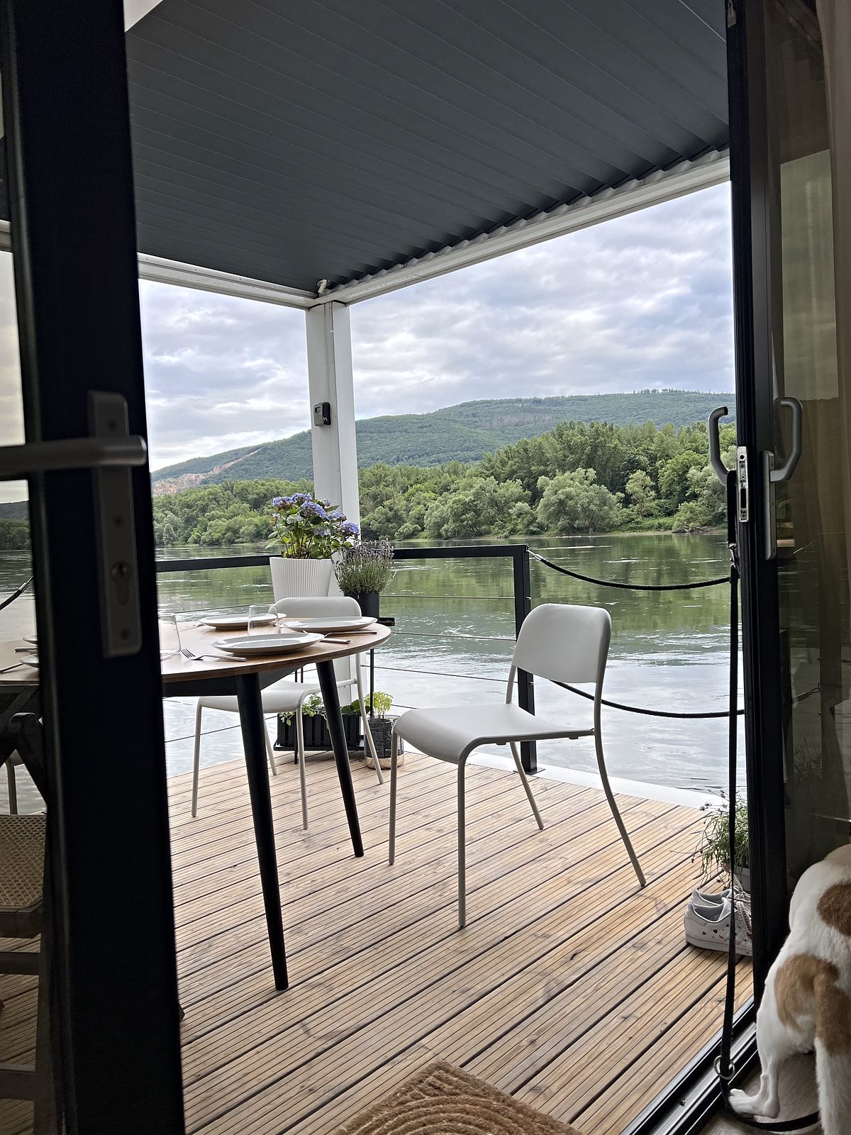 Blick aus dem Wohnraum durch die geöffnete Schiebetür auf die Holzterrasse und den Rhein.