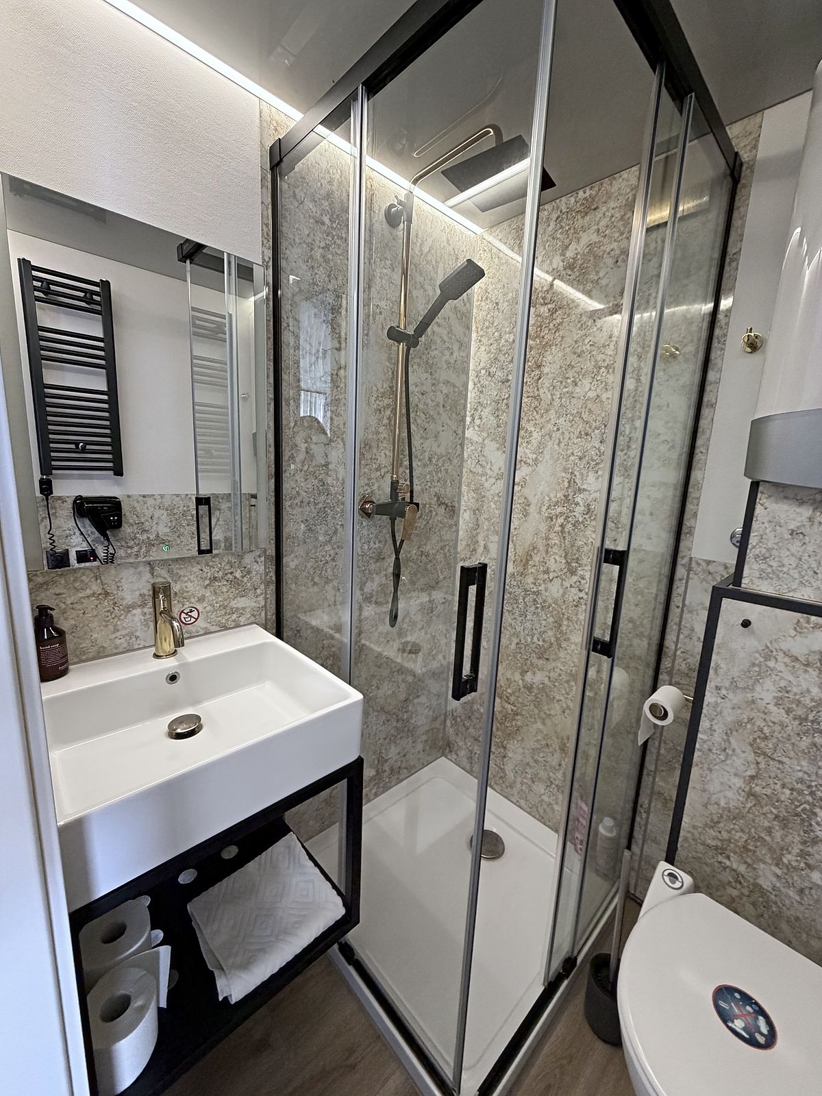 Badezimmer mit ebenerdiger Dusche, Waschtisch und Handtuchheizkörper.