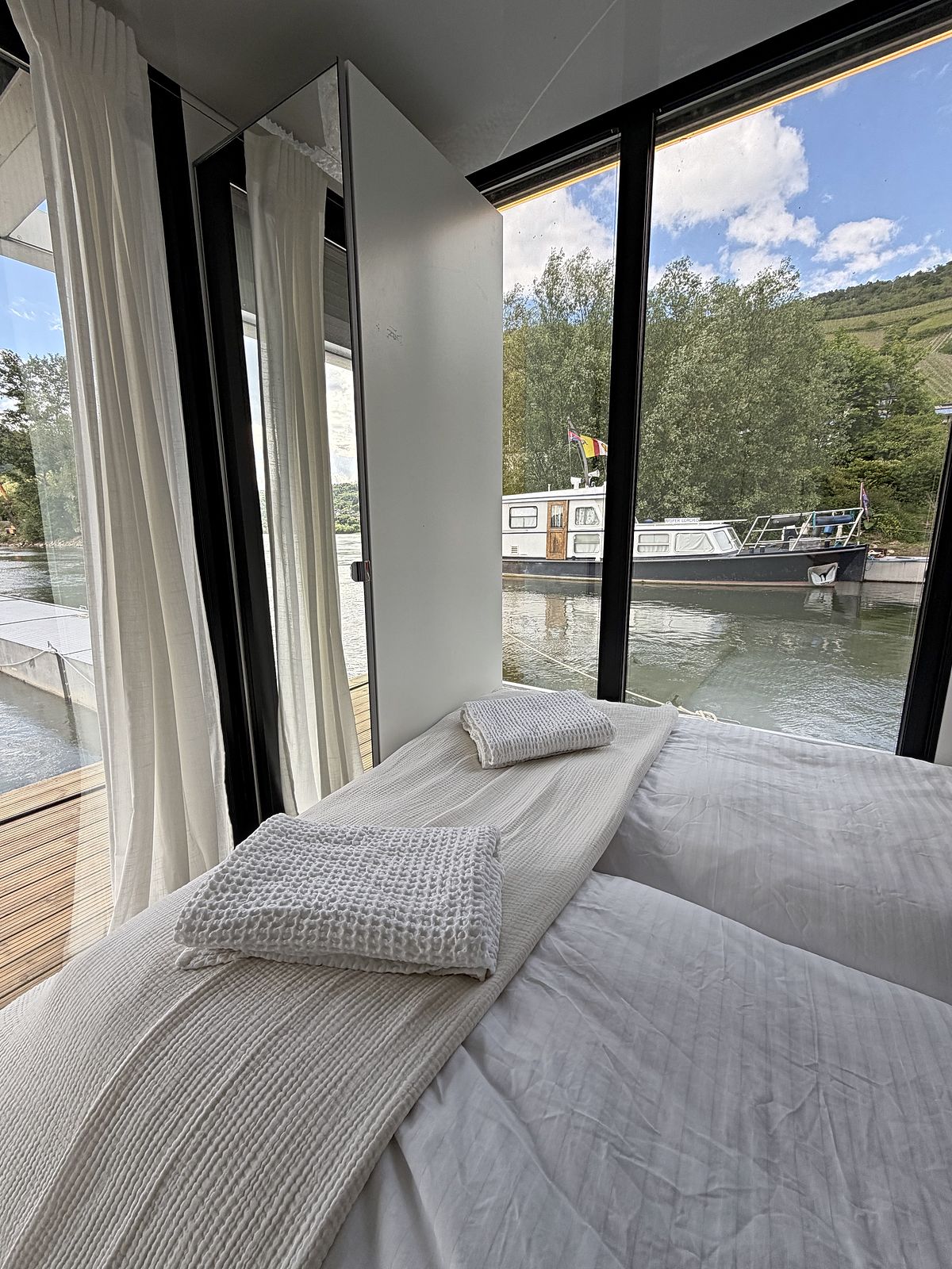 Schlafzimmer mit Doppelbett, weißer Bettwäsche und Fenster mit Blick auf das Wasser.