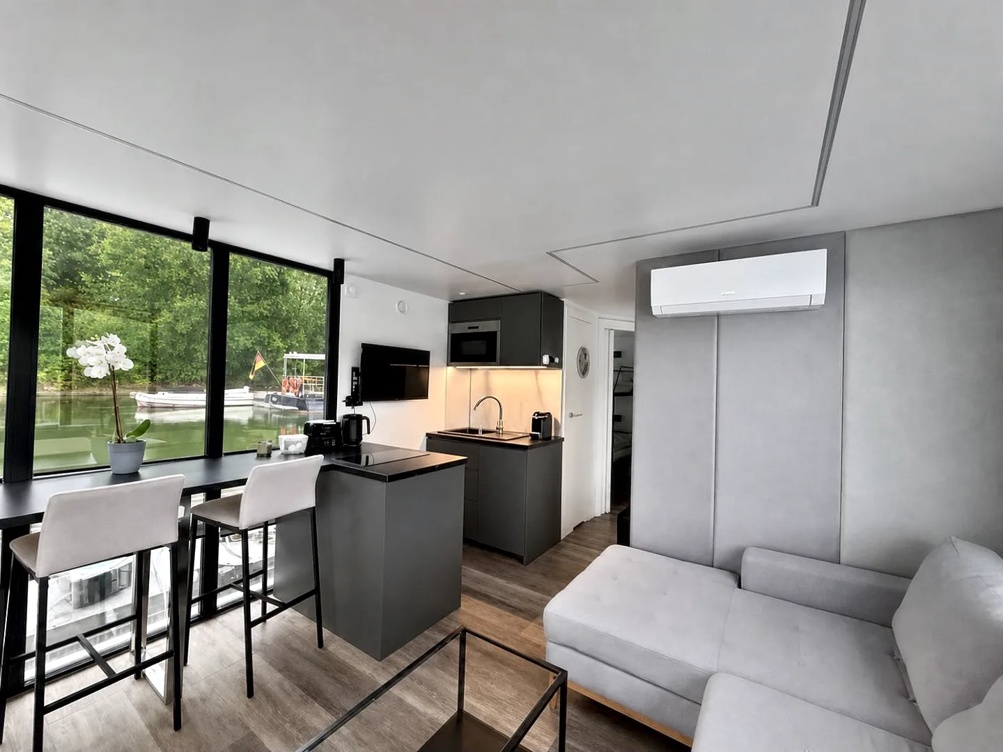 Wohnraum von Modern 1: anthrazitfarbene Küchenzeile mit Kochinsel, Barhocker am Fenster und graue Polstergruppe.