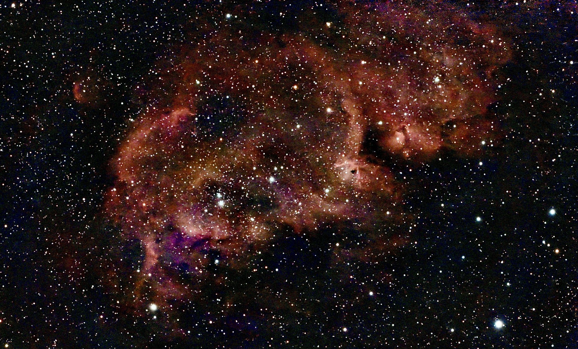 Ein ausgedehnter roter Emissionsnebel mit eingebettetem Sternhaufen und dunklen Staubfäden.