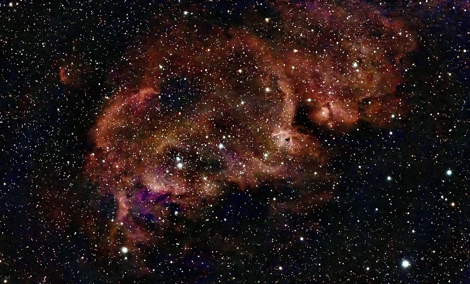 Ein ausgedehnter roter Emissionsnebel mit eingebettetem Sternhaufen und dunklen Staubfäden.
