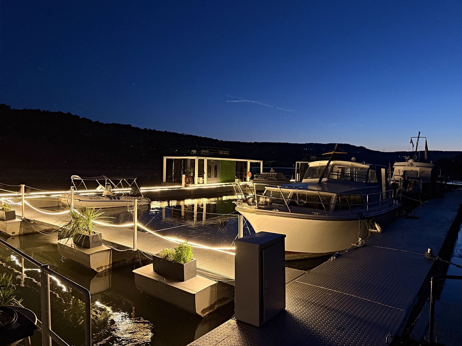Beide Hausboote bei Nacht, das Licht der Stegbeleuchtung zieht eine Linie über das Wasser.