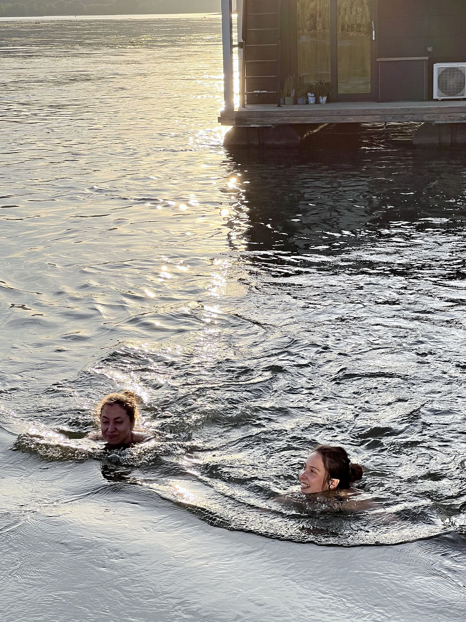 Zwei Gäste schwimmen im Rhein neben dem Hausboot.
