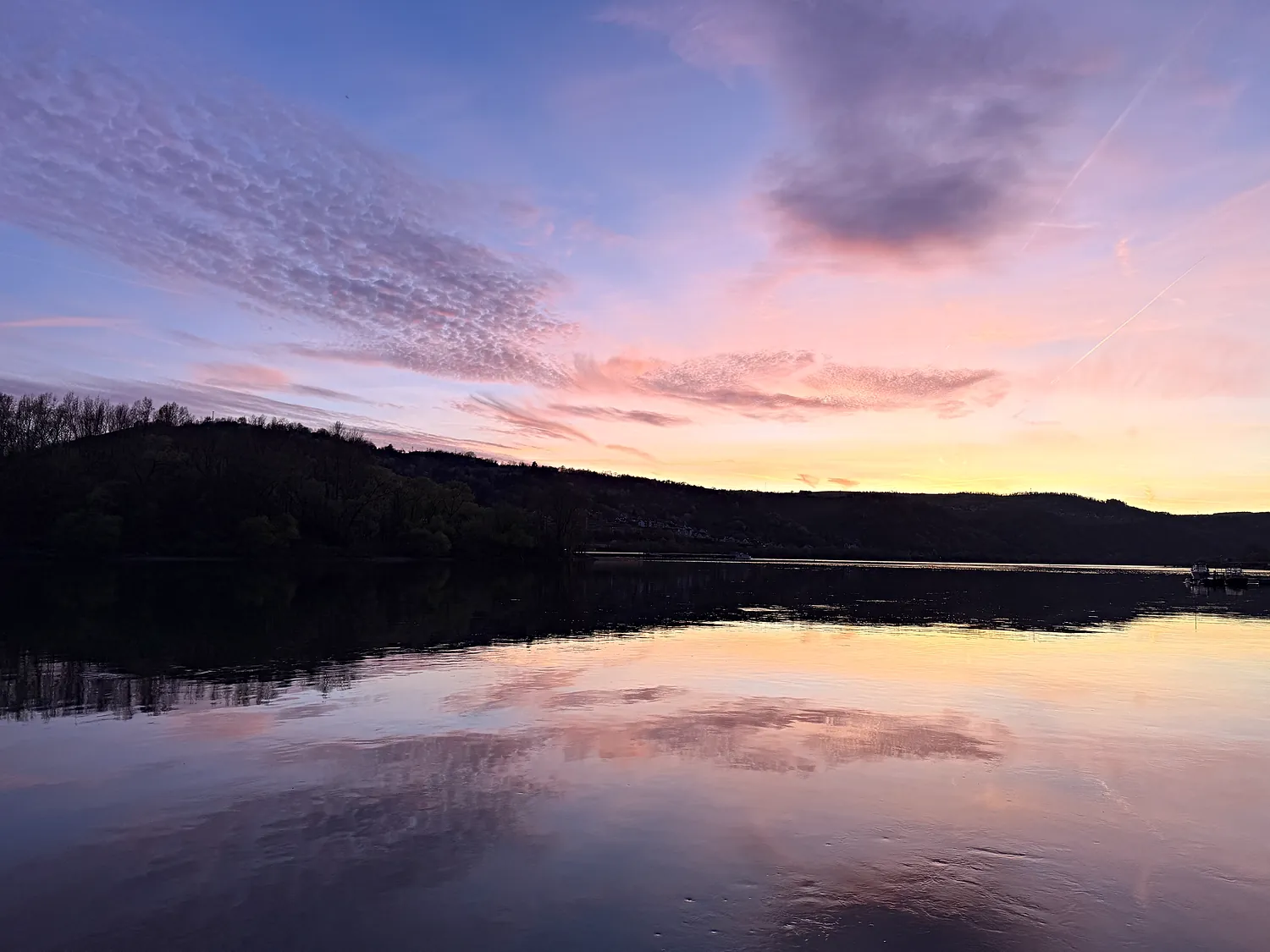 Rosafarbene Abendwolken über dem Rhein, das Wasser liegt spiegelglatt.
